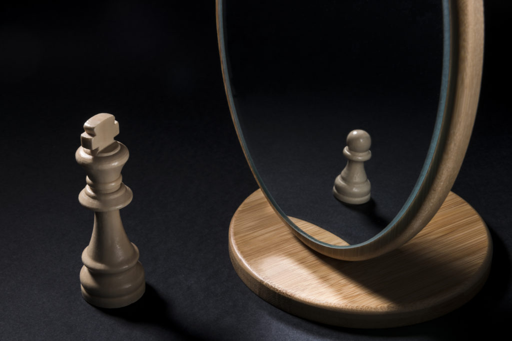 A king seeing itself as a pawn in a mirror. They see themselves as something different which is hindering their success. 
